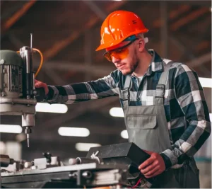 A mechanical technician wearing an orange hard hat and safety glasses, focused on inspecting or setting up an industrial milling machine in a workshop, illustrating reliable engineering solutions.